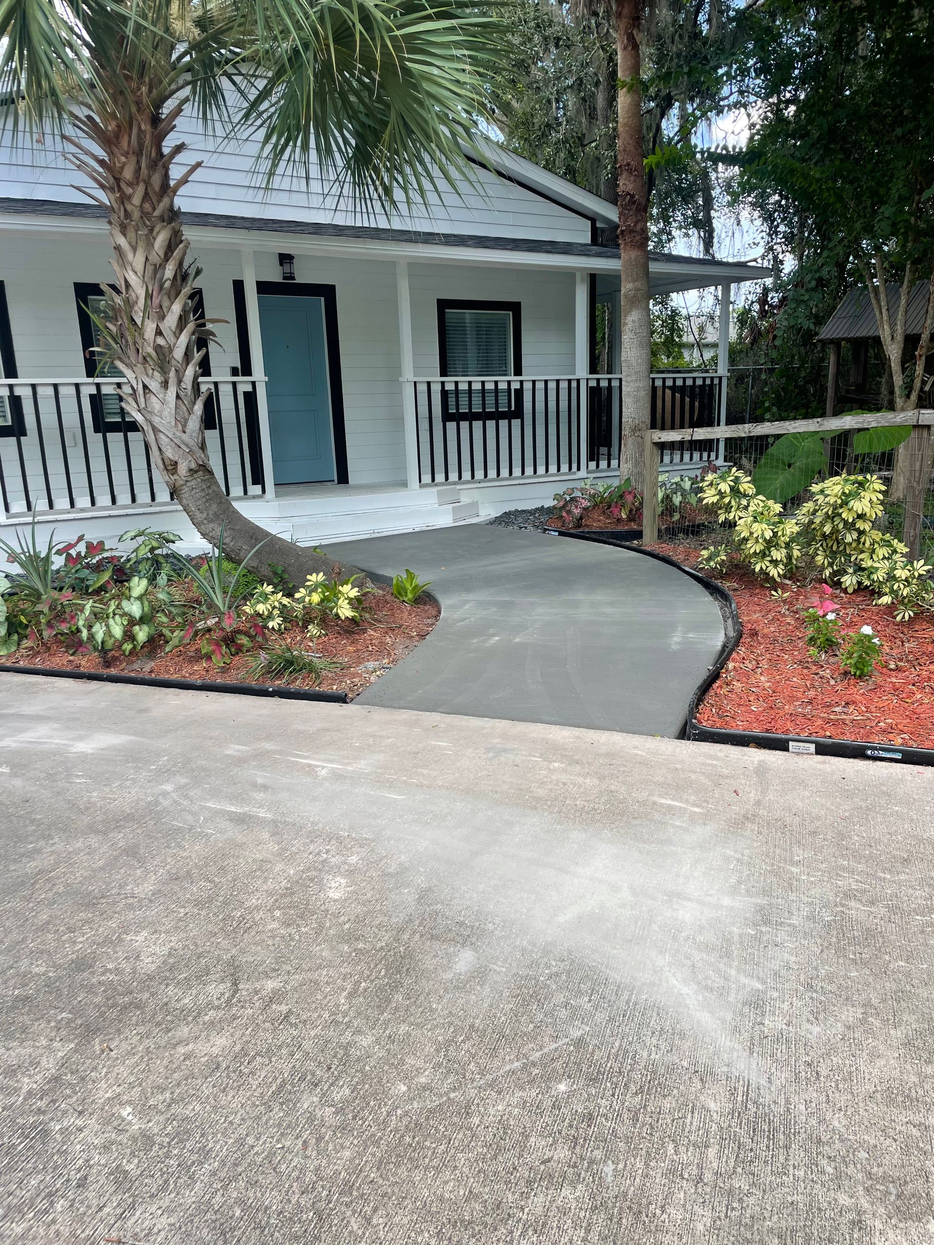 Exterior of a white house with a curved pathway, bordered by red mulch and landscaping.