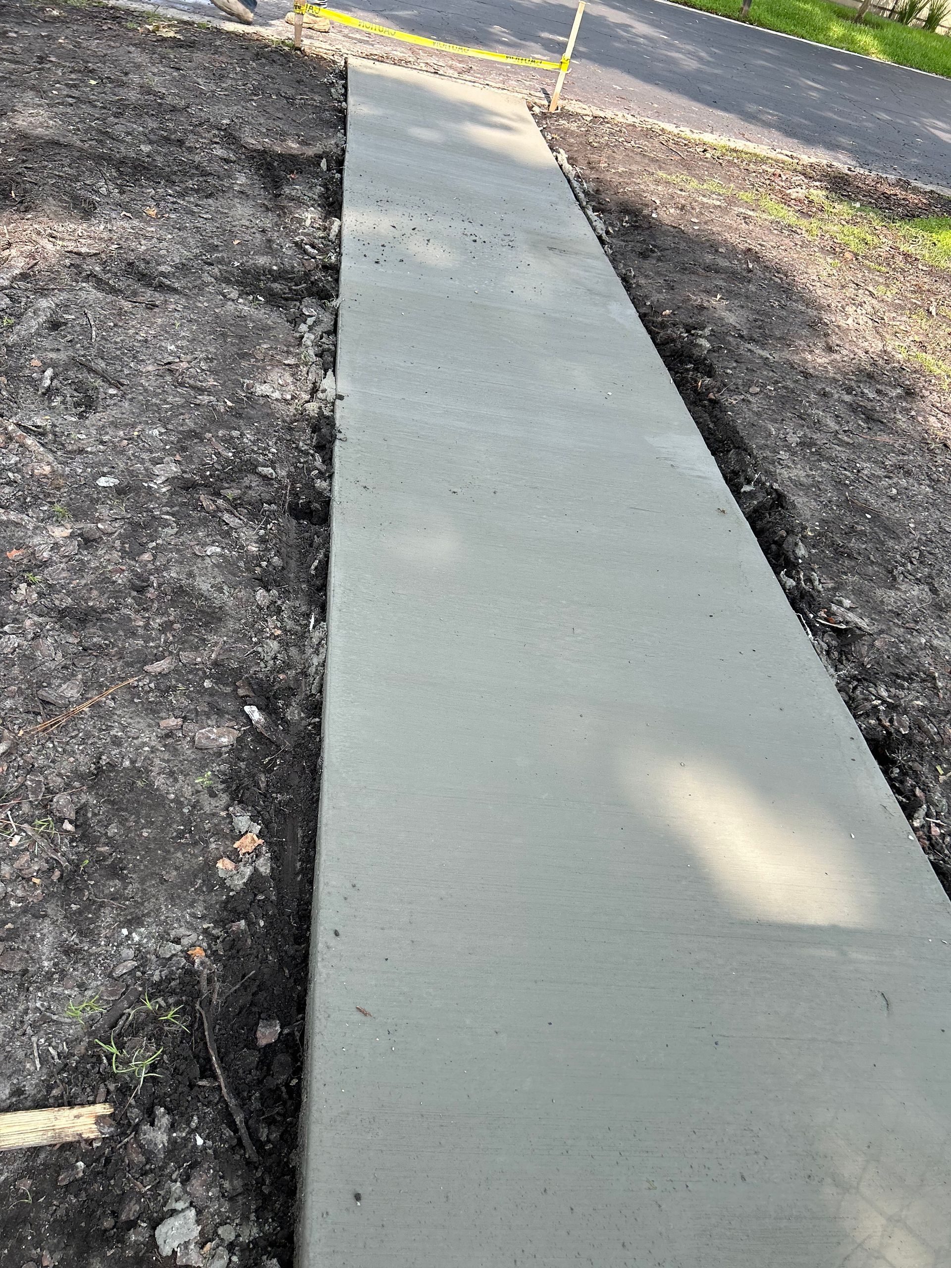 Newly poured gray concrete sidewalk in a dirt yard.