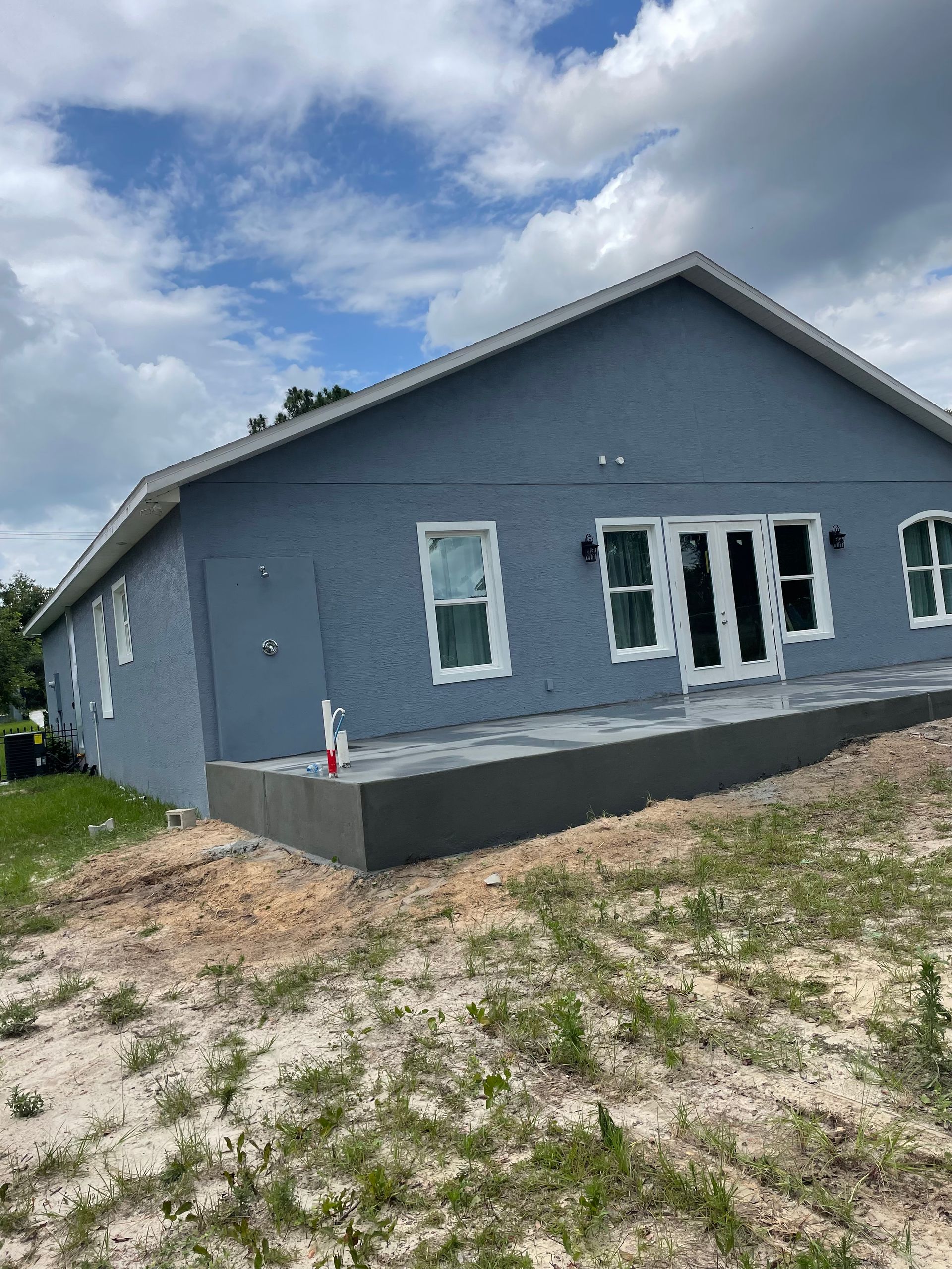 Outdoor seating area with a wooden bench, white walls, and a tree.