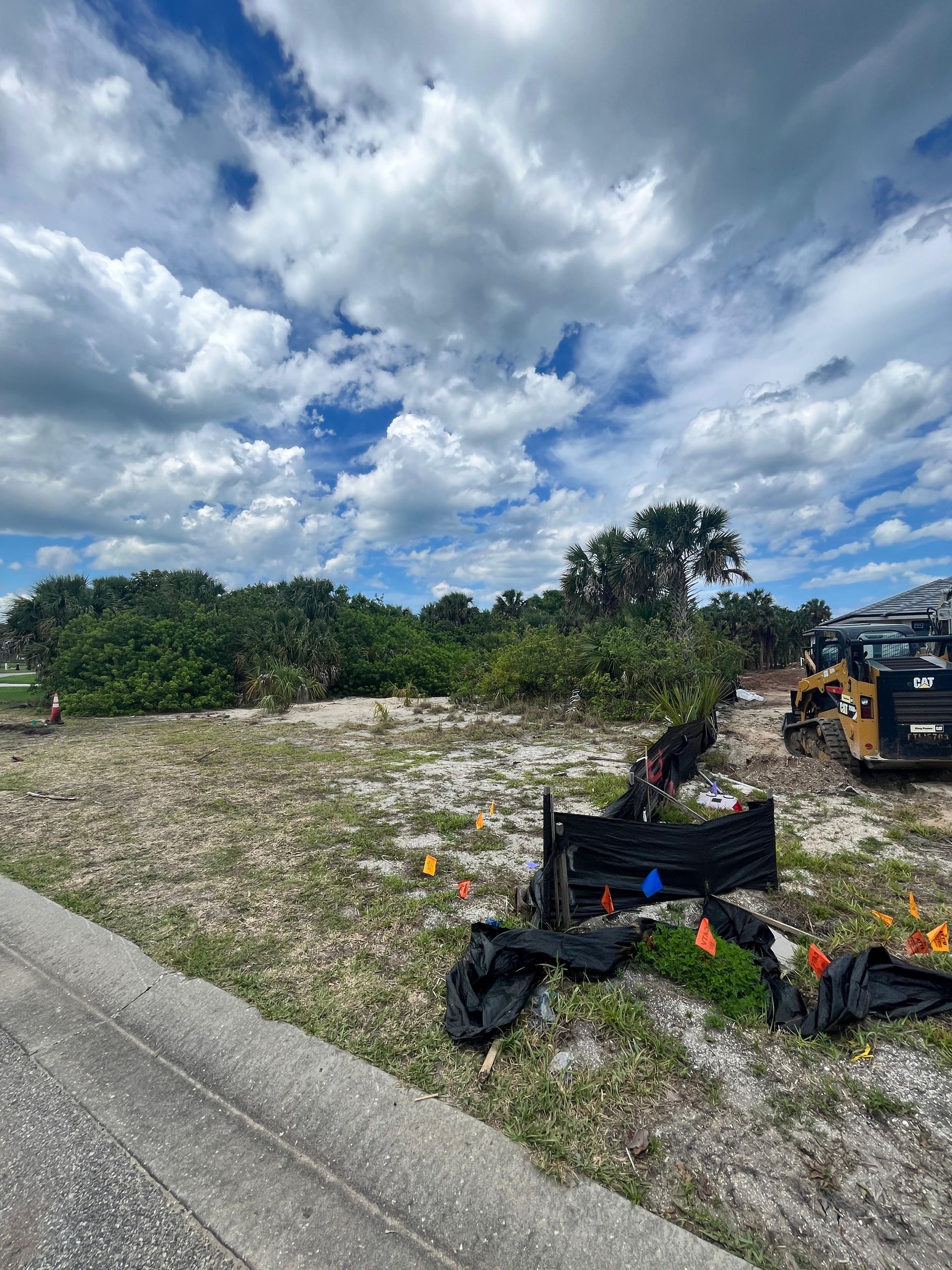 Construction site with cloudy sky, dirt, trees, and a skid steer.