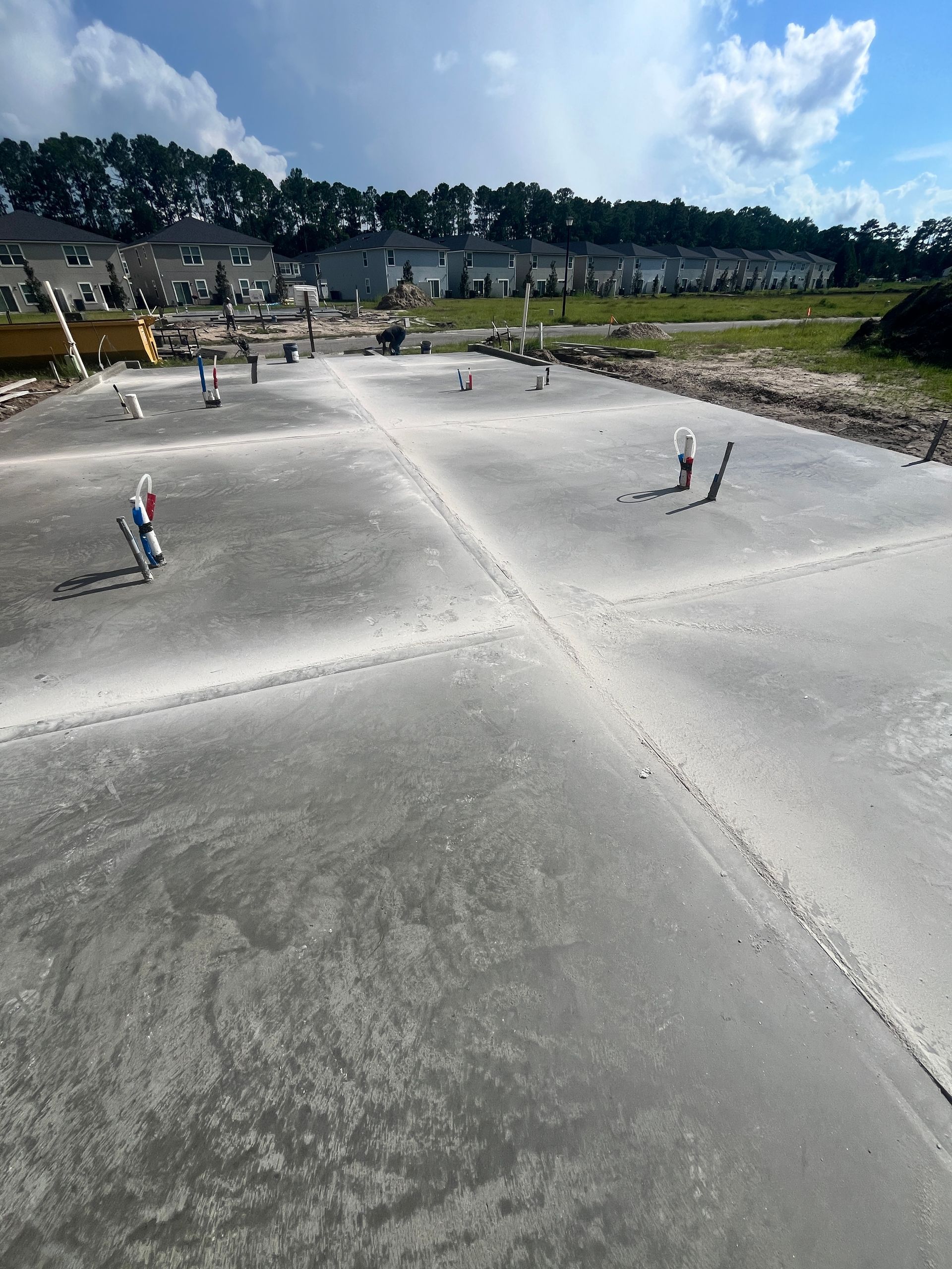 Newly poured concrete foundation with plumbing pipes in a construction site.