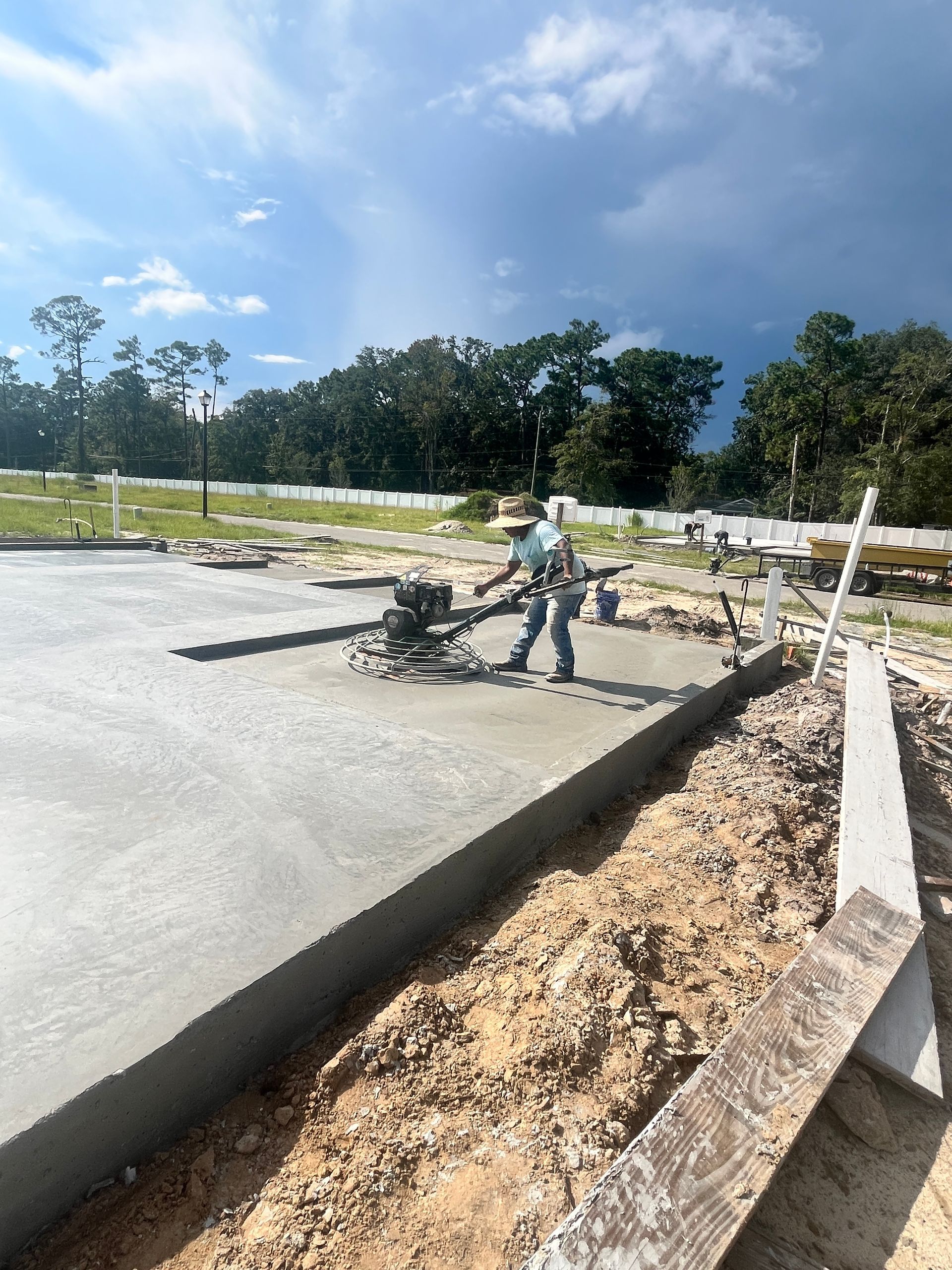 Construction worker smoothing wet concrete on a foundation, sunny day.