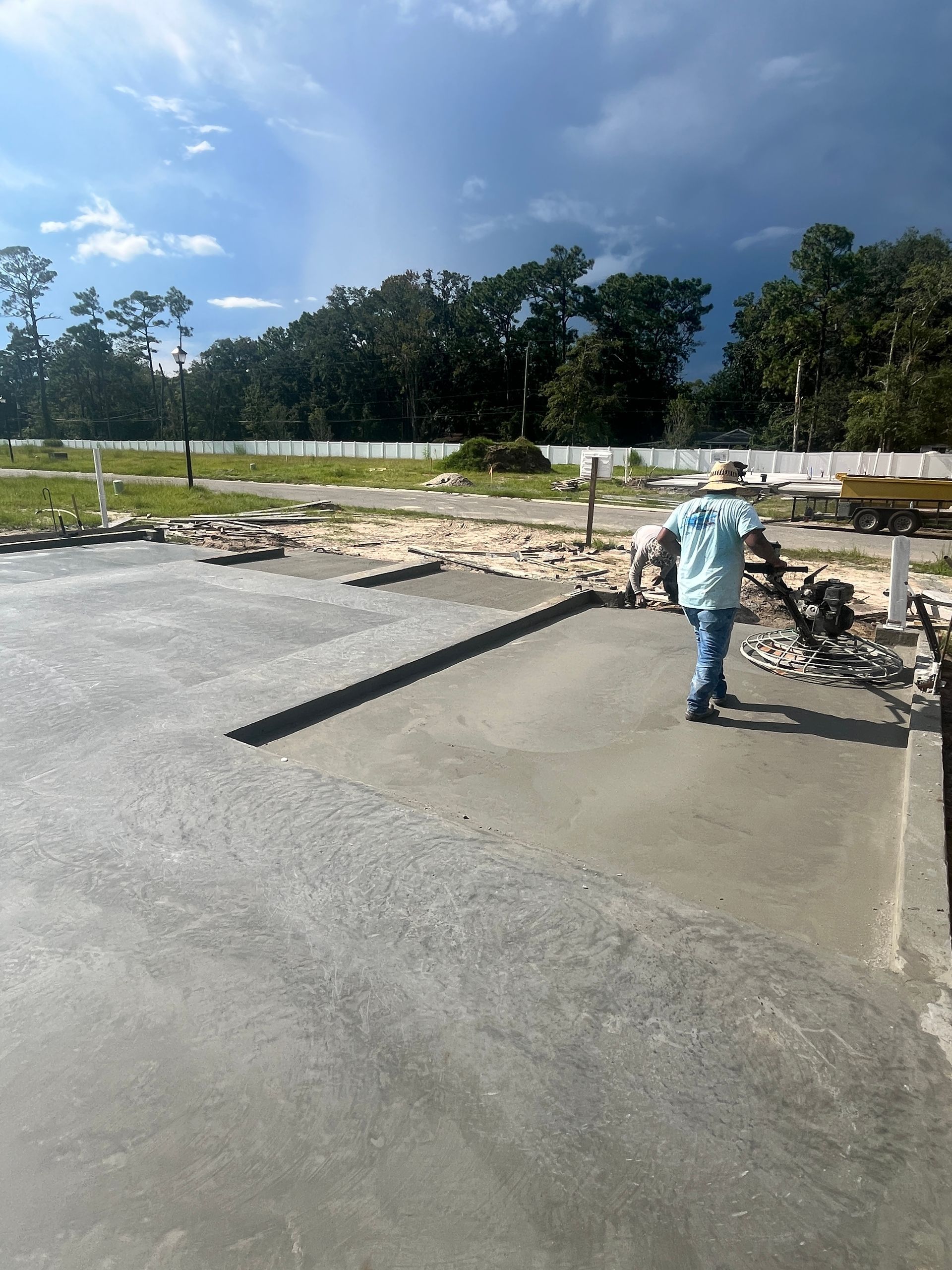 Man finishing a freshly poured concrete slab outdoors on a cloudy day.