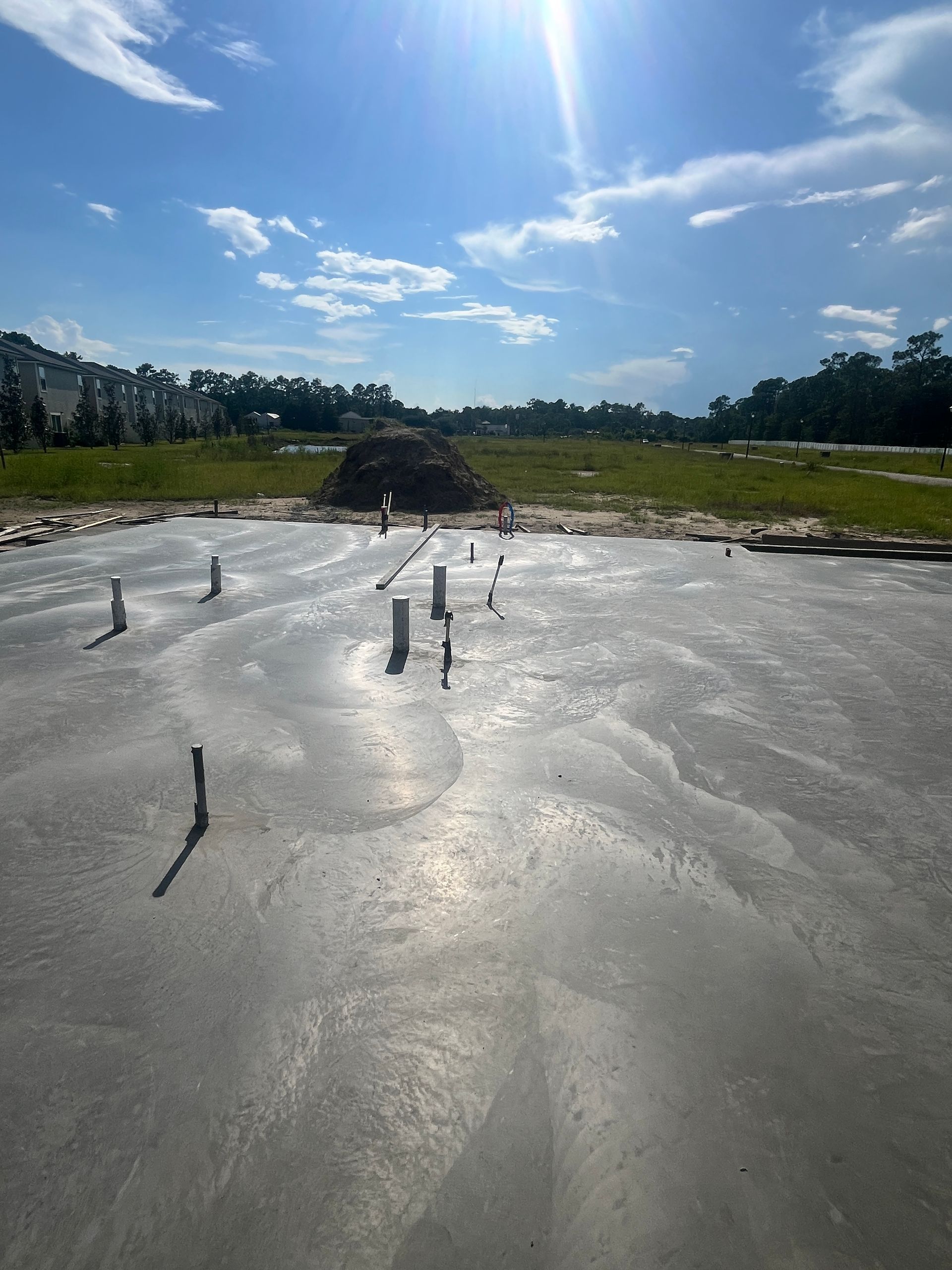 Newly poured concrete foundation with plumbing pipes, sunny day.