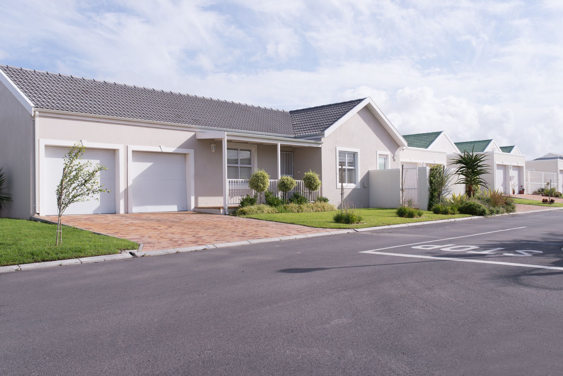 Row of modern houses with gray roofs and white garages on a sunny street.