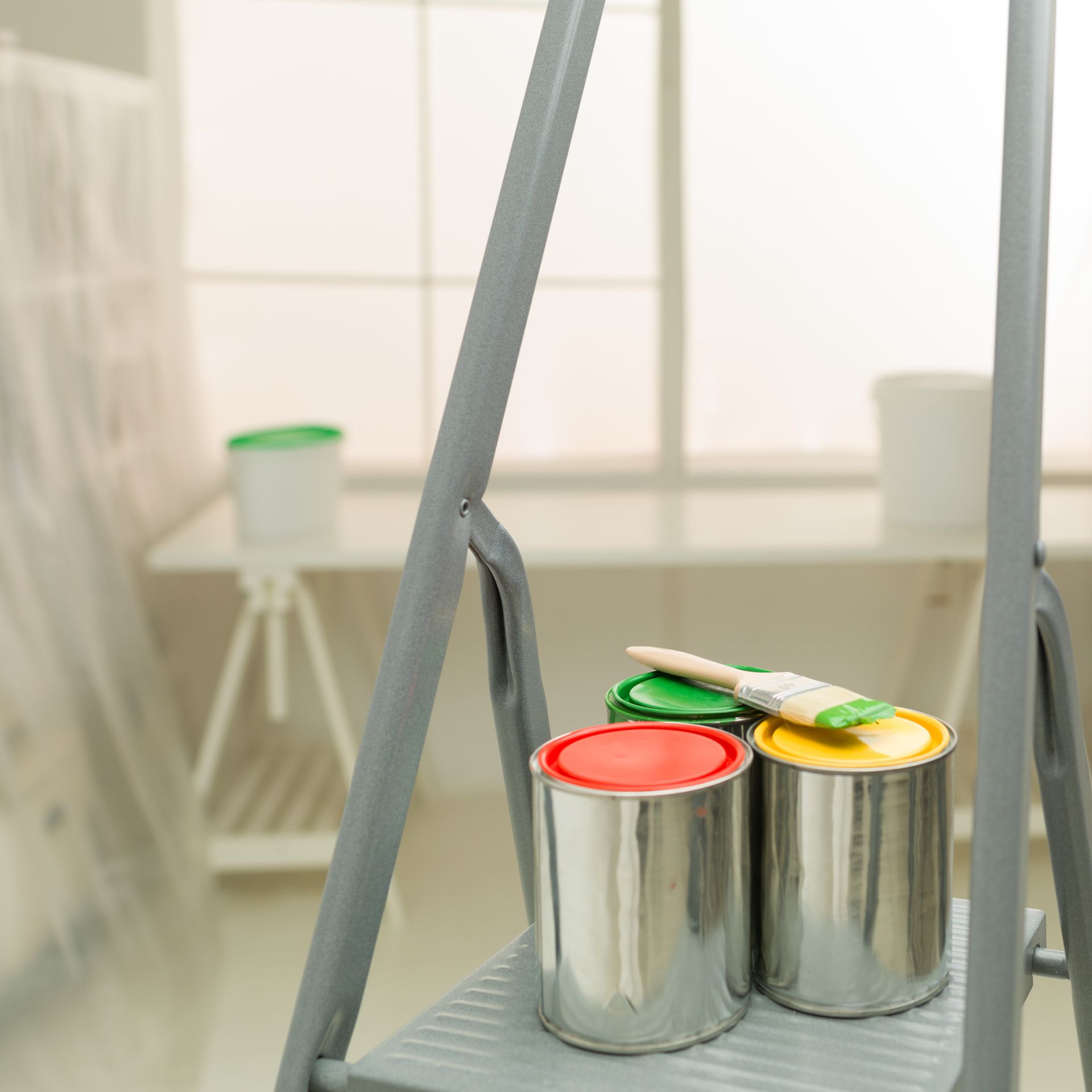 Three cans of paint and a brush on a ladder