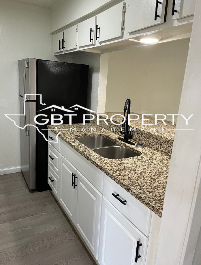 A kitchen with granite counter tops , white cabinets , a sink and a refrigerator.