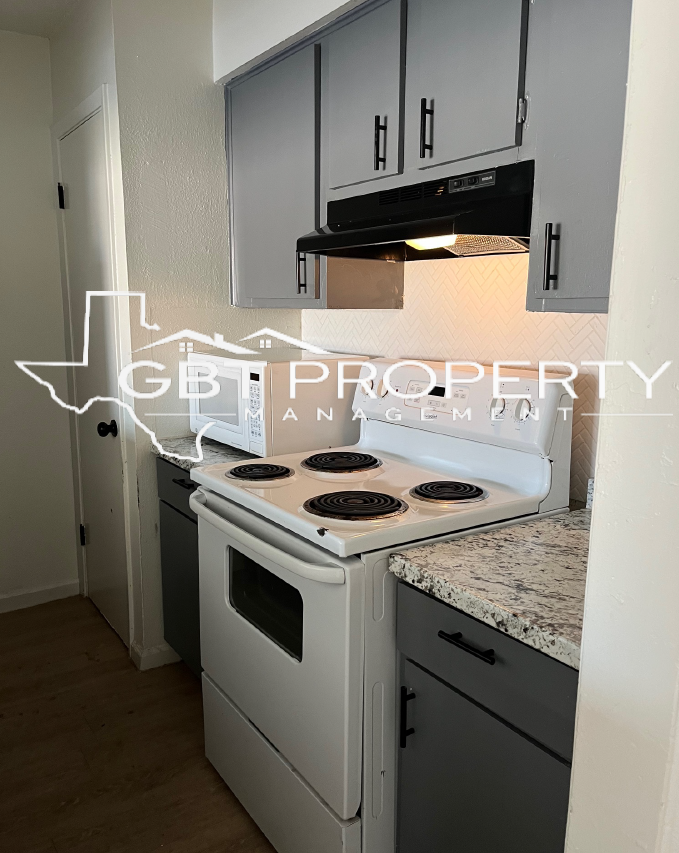 A kitchen with a white stove top oven and gray cabinets.