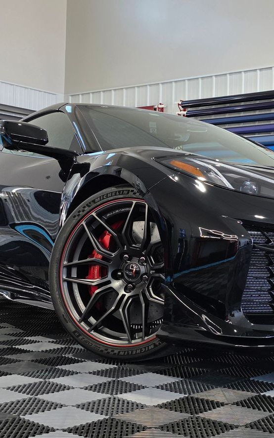 A person applying a lavender vinyl wrap to a car door in a well-lit garage.