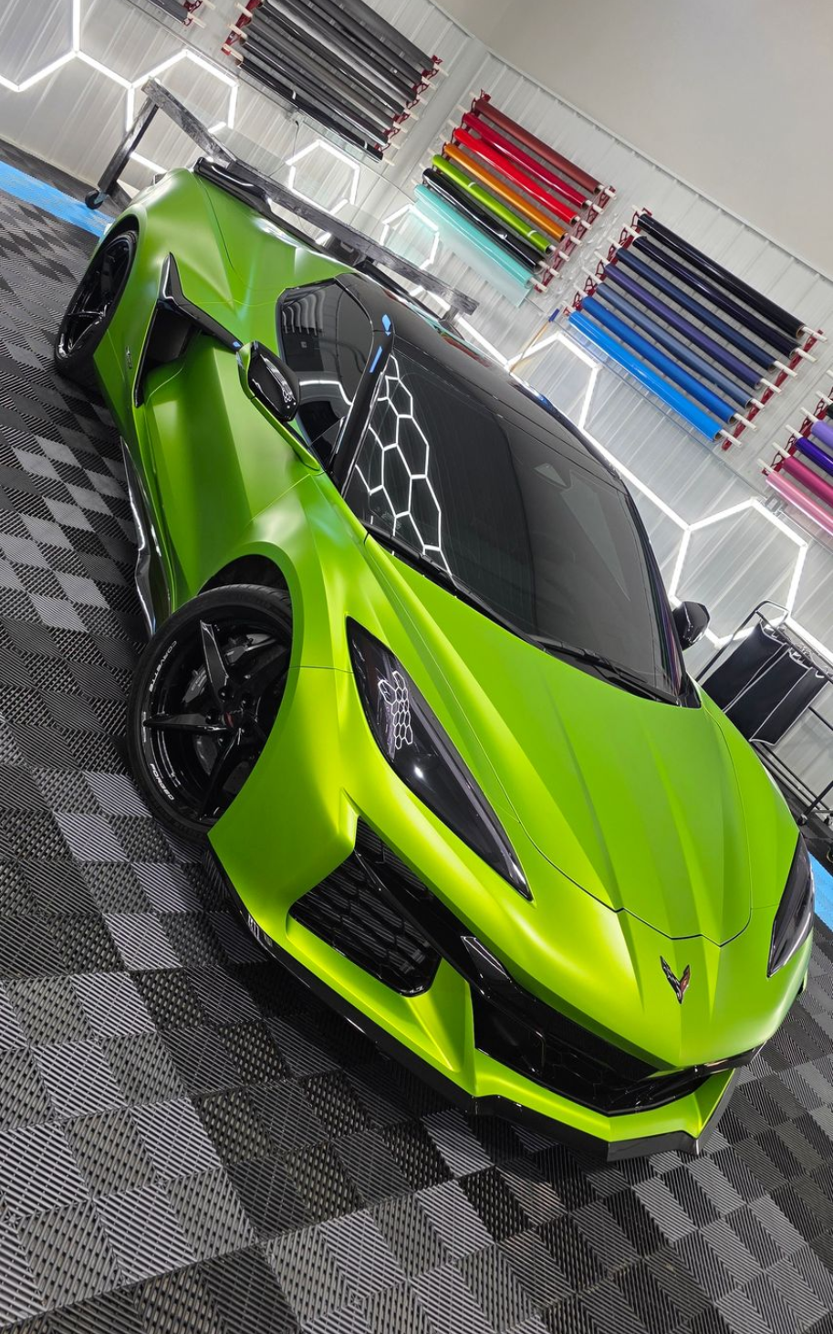 Bright green sports car in a shop, with black wheels, wing, and roof.