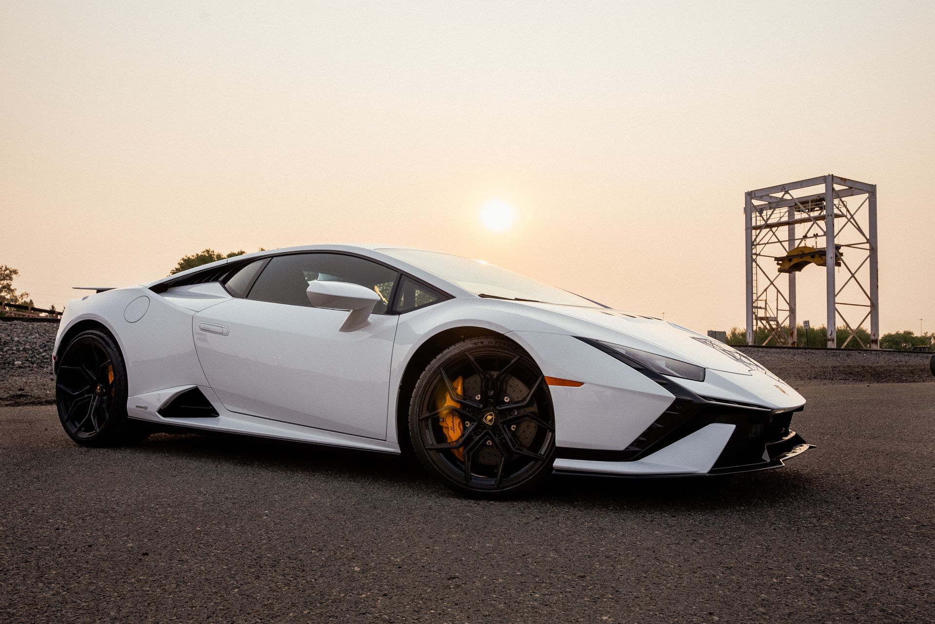 White Lamborghini sports car parked on asphalt, setting sun in the background.
