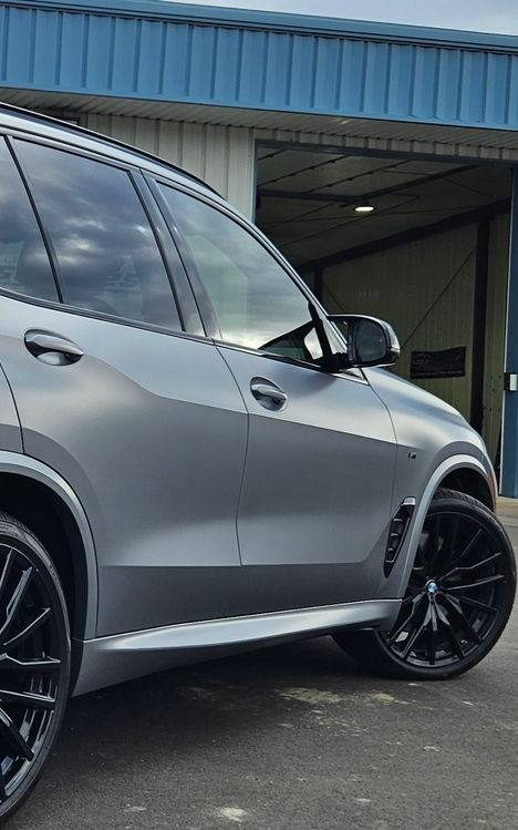 Gray SUV with black rims parked outside a building with a blue facade and open garage door.
