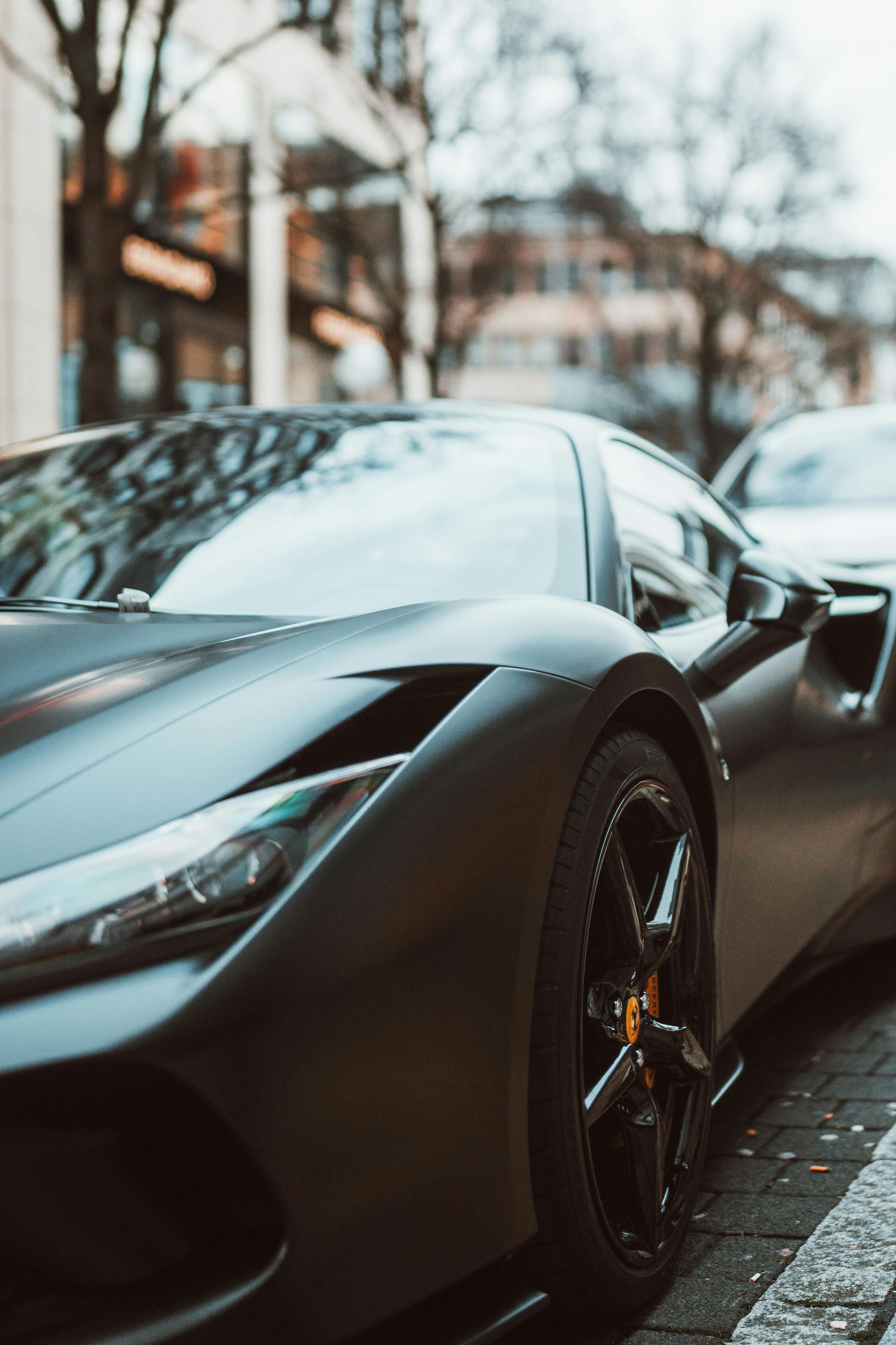 Dark gray sports car parked on a city street, with black wheels and a building background.