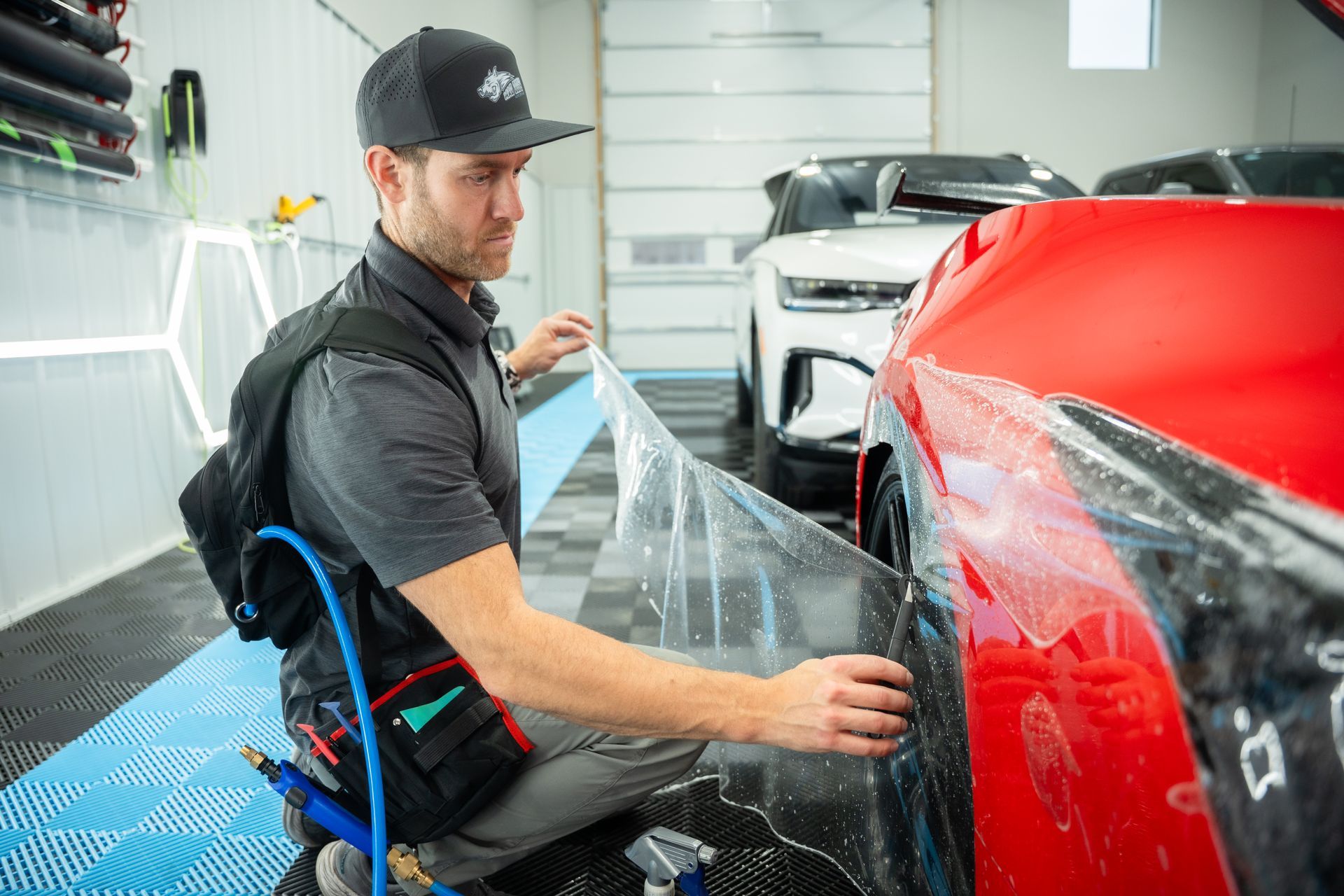 Man applying protective film to a red car in a garage.