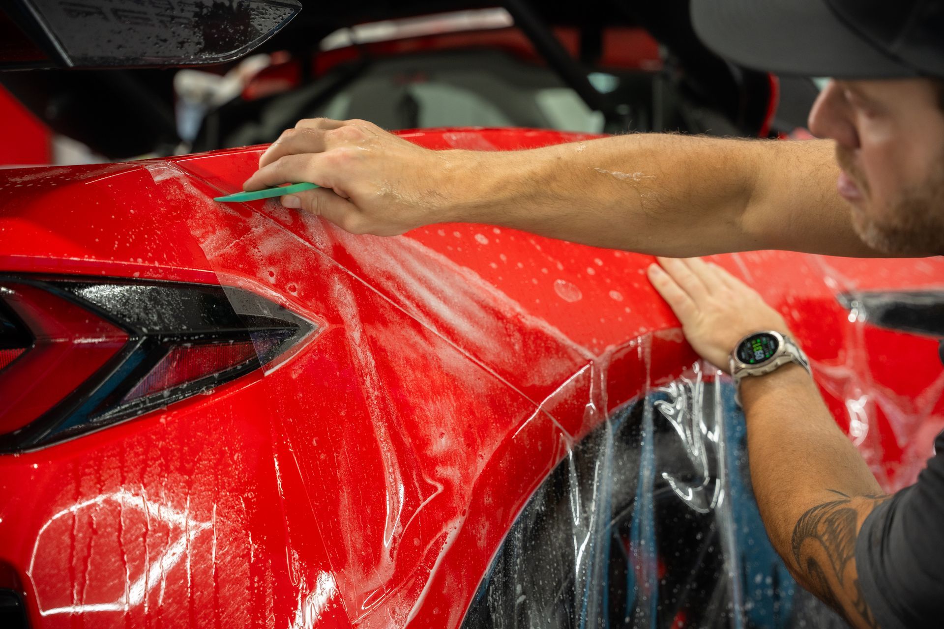 Person applying film to red car fender. Close-up with squeegee and soapy water.