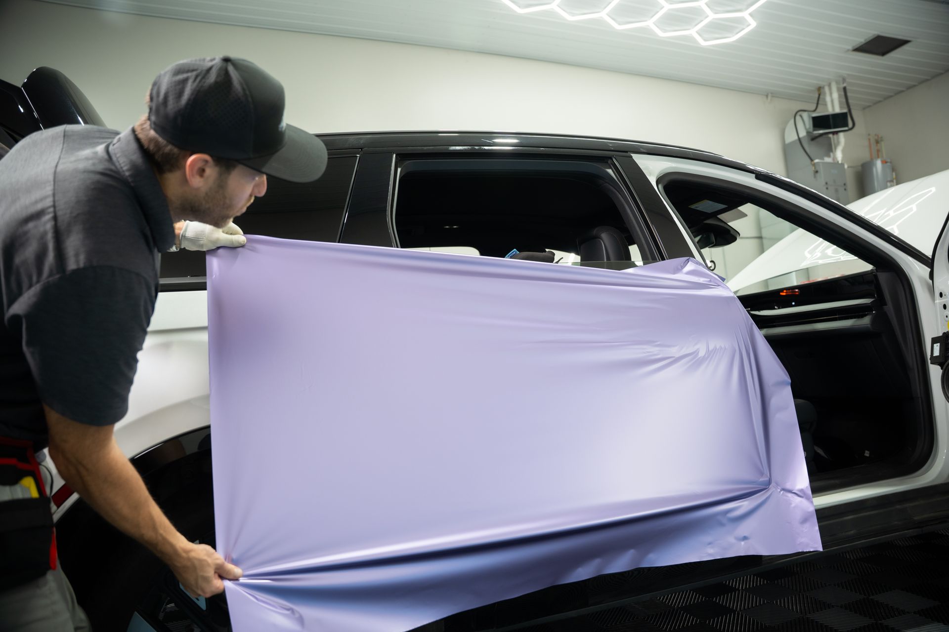 Person applying lavender vinyl wrap to a car door in a shop.