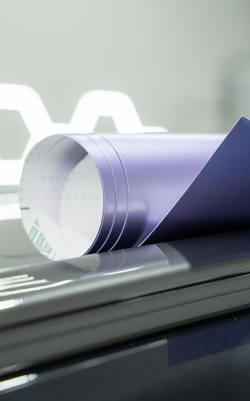 Rolled-up purple vinyl wrap on a dark surface, with a white, honeycomb-shaped light source in the background.
