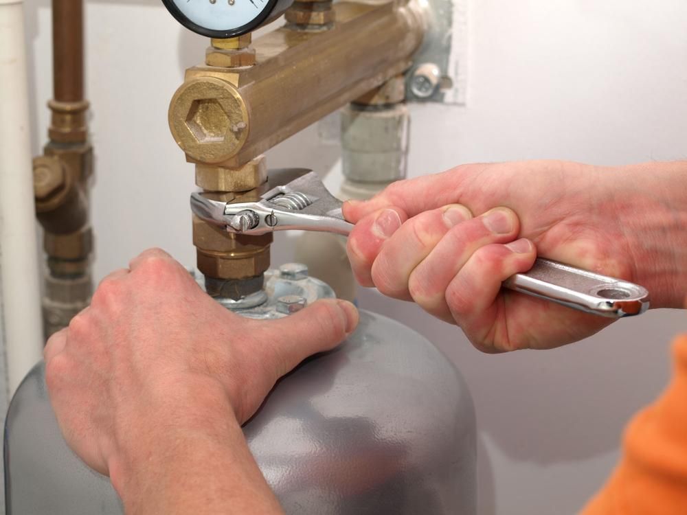 A Person Is Fixing a Water Heater with A Wrench — Delaney Plumbing Services In Taree, NSW