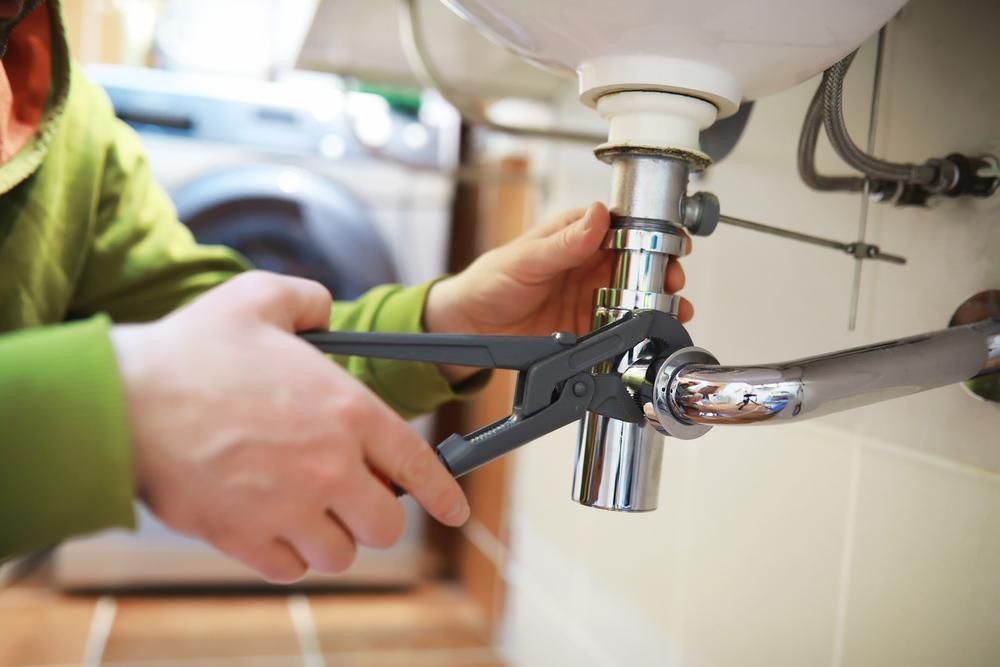 A Person Is Fixing a Sink with A Wrench — Delaney Plumbing Services In Taree, NSW