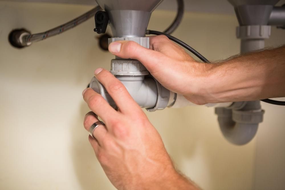 A Person Is Fixing a Sink Pipe Under a Sink — Delaney Plumbing Services In Taree, NSW