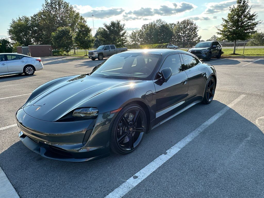 A black porsche taycan is parked in a parking lot.