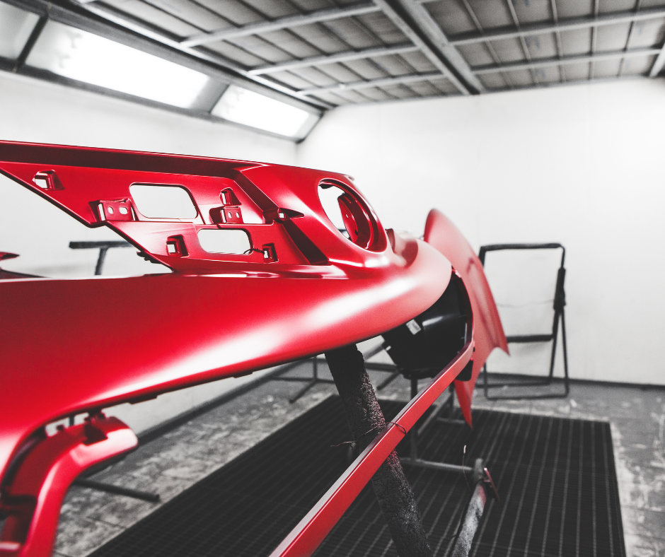 A red car is being painted in a paint booth