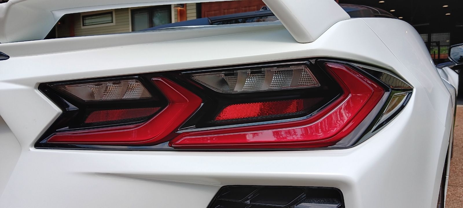 A white sports car with a red tail light is parked in front of a house.