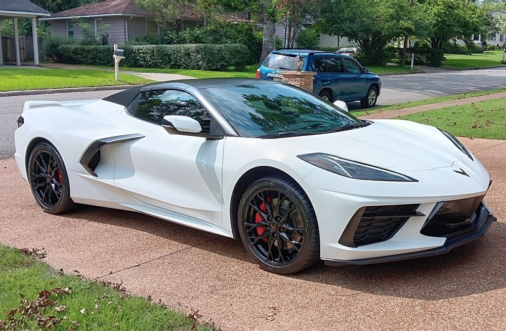 A white sports car is parked in a driveway next to a house.
