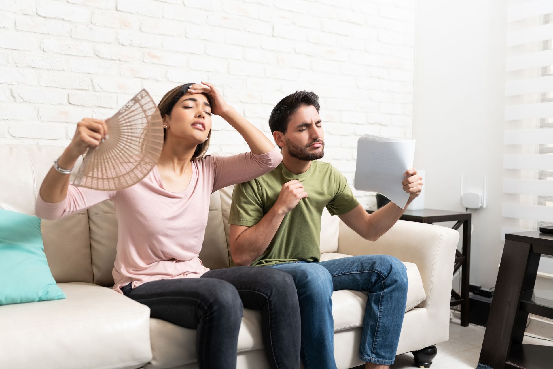 A man and a woman are sitting on a couch holding fans.