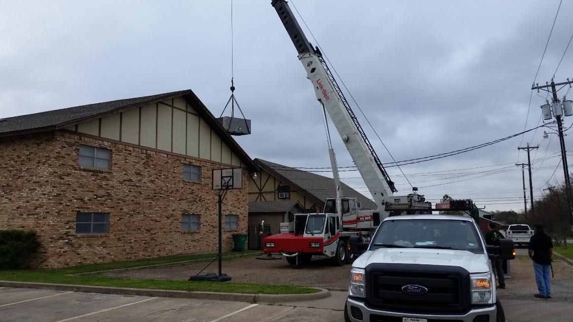 A truck is parked in front of a building with a crane lifting a box.