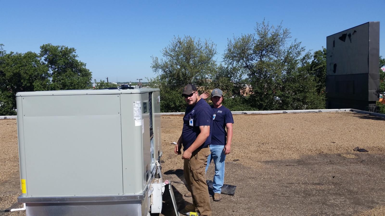 A man is standing on a roof watching a crane lift a piece of equipment.