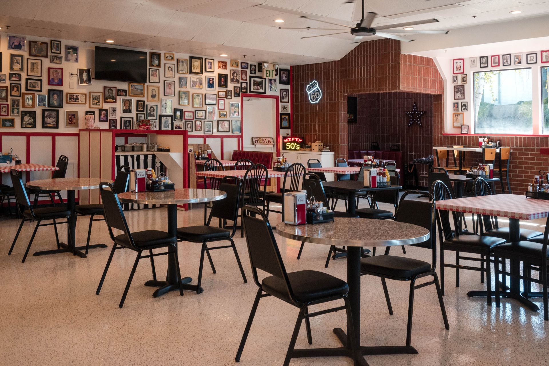 Empty café with scattered black chairs and tables, walls covered in framed photos and a red-lit corner booth