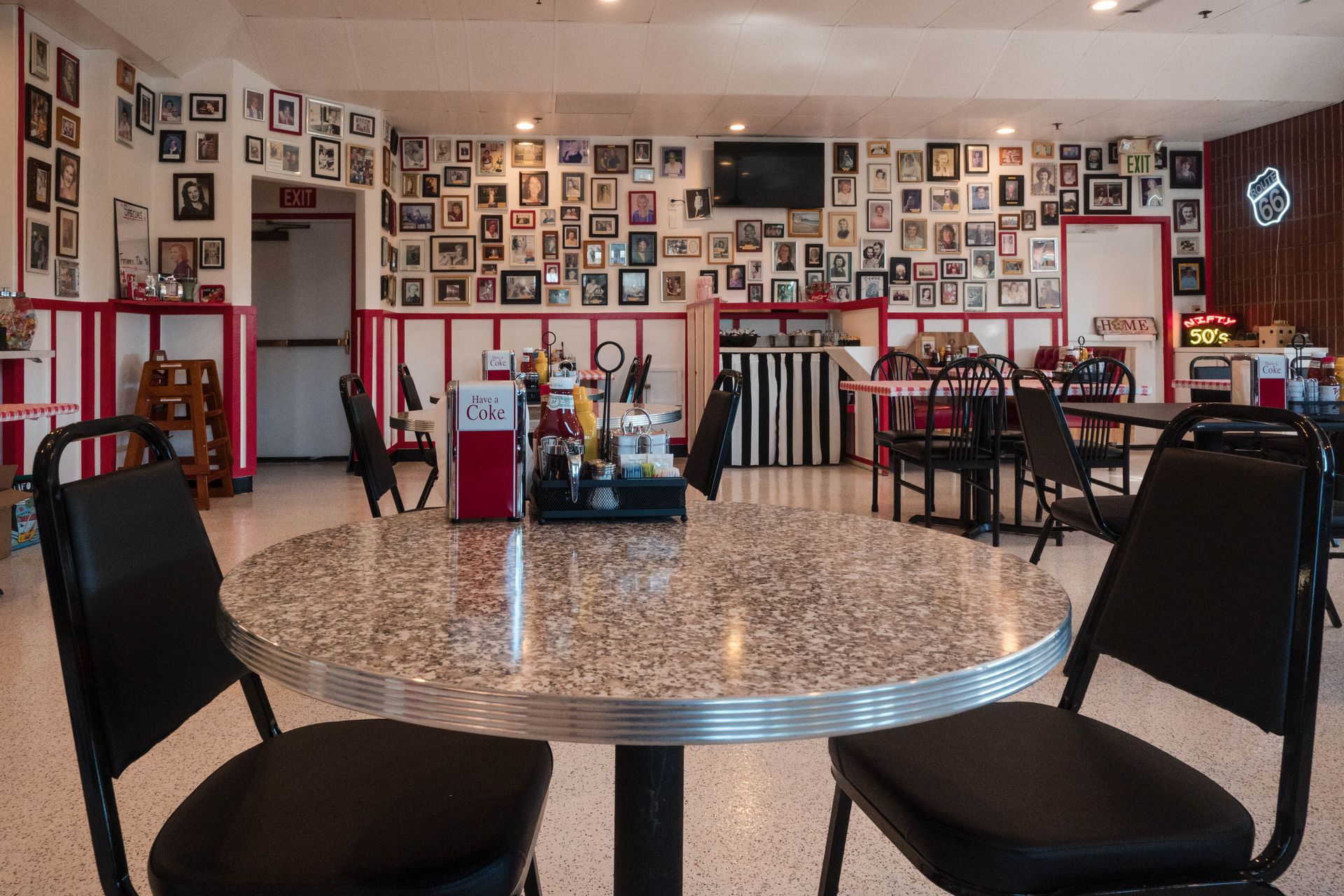Empty cafe interior with mosaic floor, framed photos on walls, and round tables with black chairs