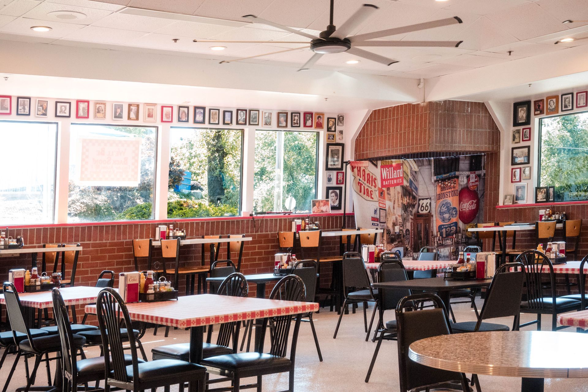 Bright classroom with tables, chairs, ceiling fans, large windows, and educational posters on the walls.