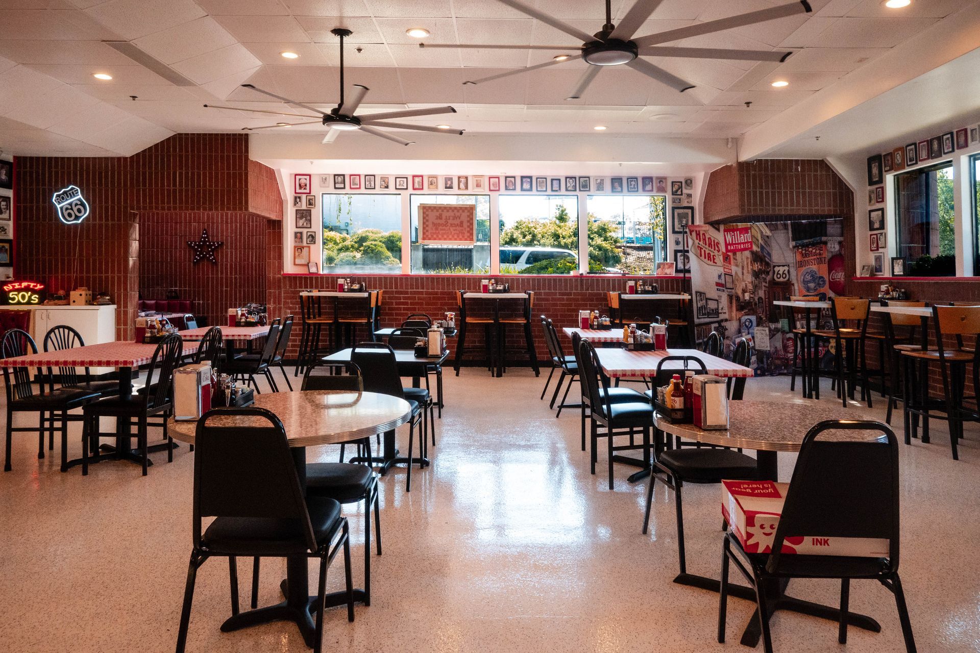 Empty restaurant dining room with tables, chairs, ceiling fans, and a front window area.