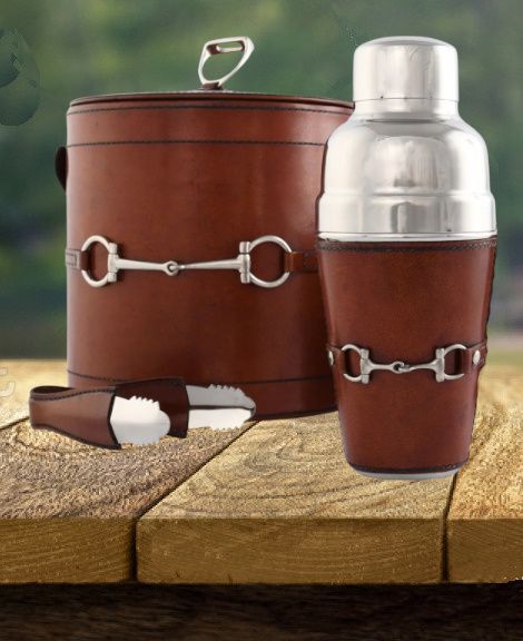 Leather-wrapped bar set with metal horse bit accents: ice bucket, cocktail shaker, and tongs on a wood surface.