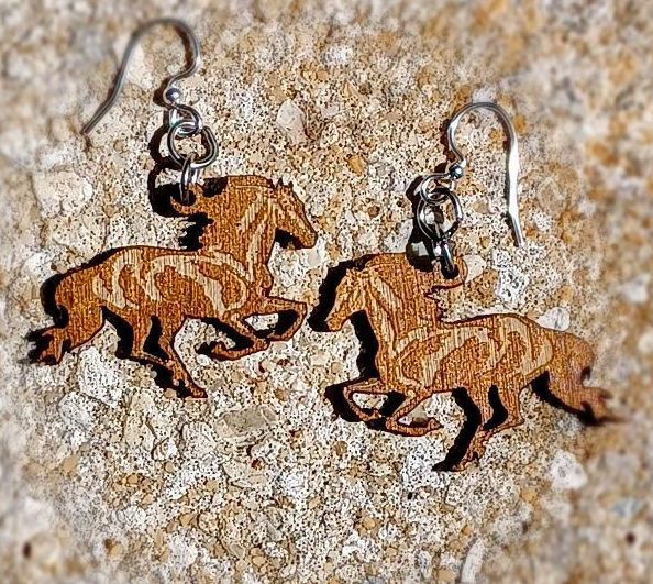 Wooden horse earrings with silver hooks on a stone surface.