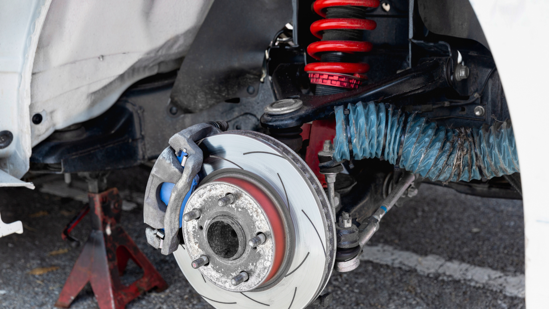 Car's suspension and brake assembly visible, including a red coil, disc brake, and other components.