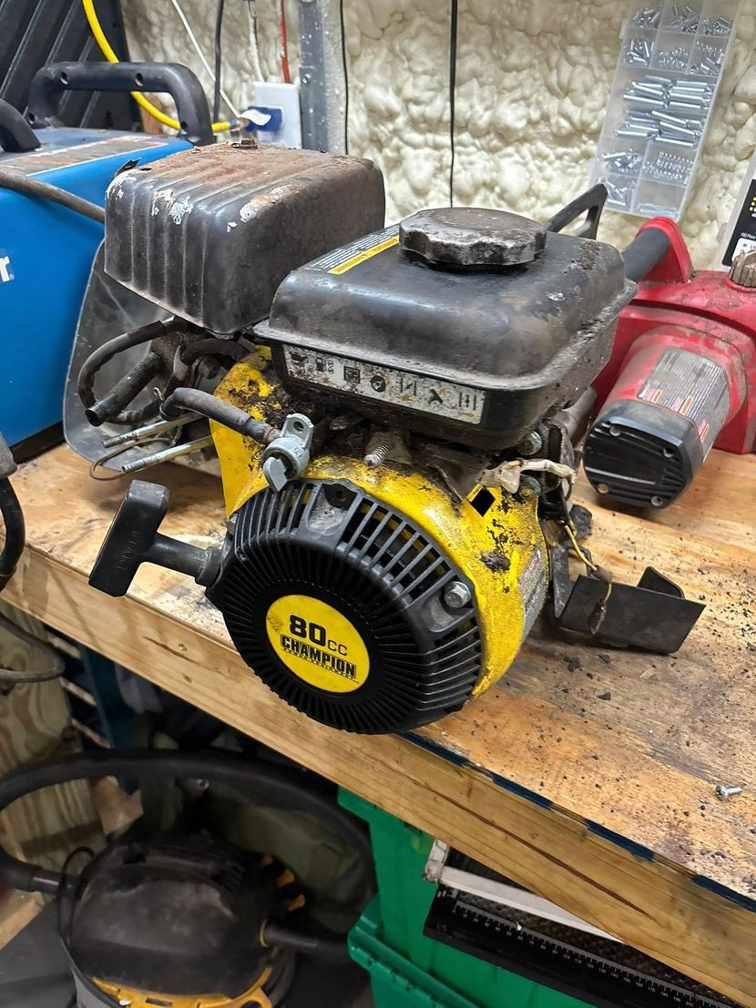 Yellow and black engine on a wooden workbench, pull start visible.