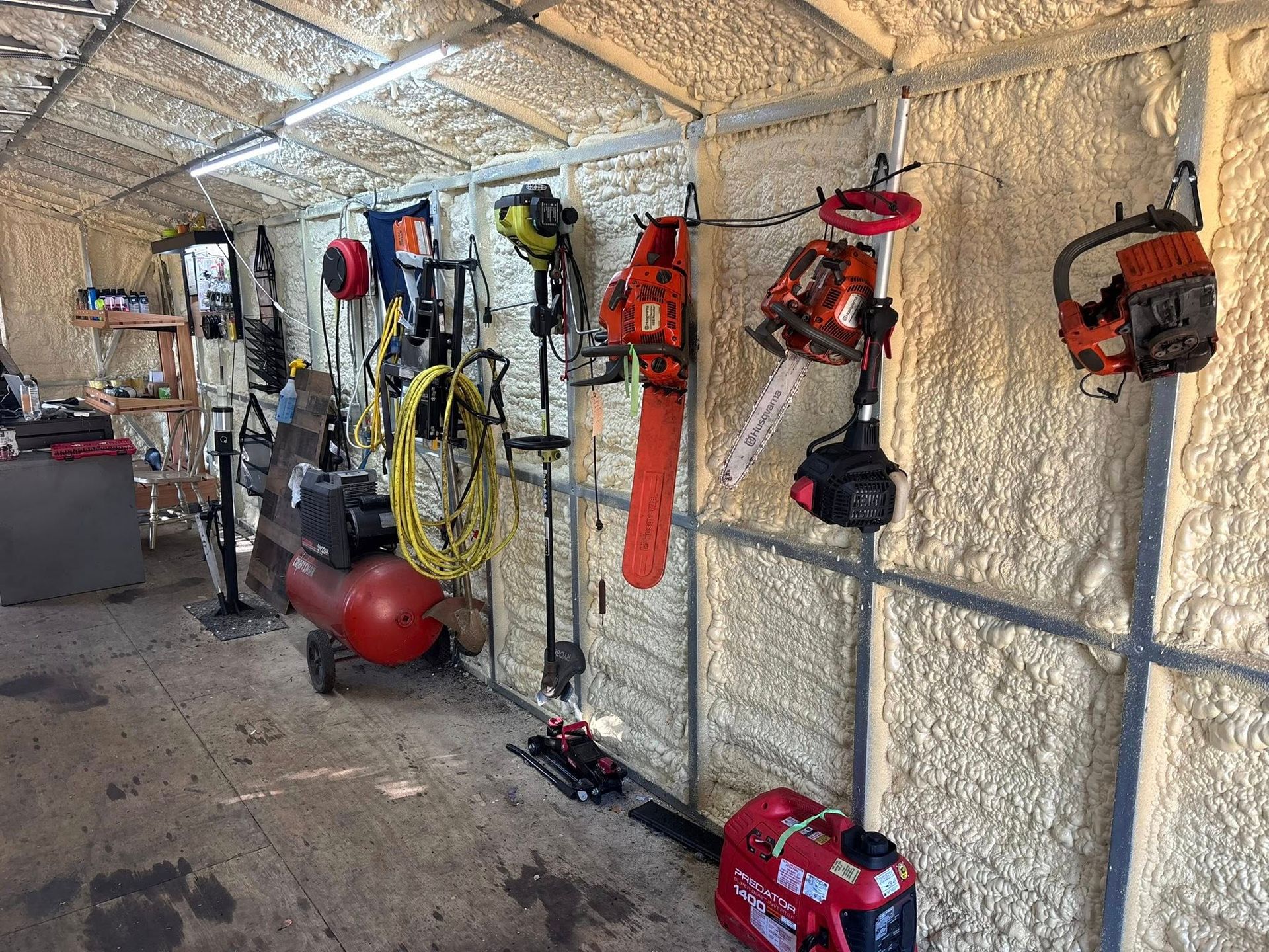 Tools hanging on a wall inside a building, including chainsaws, a compressor, and a generator.