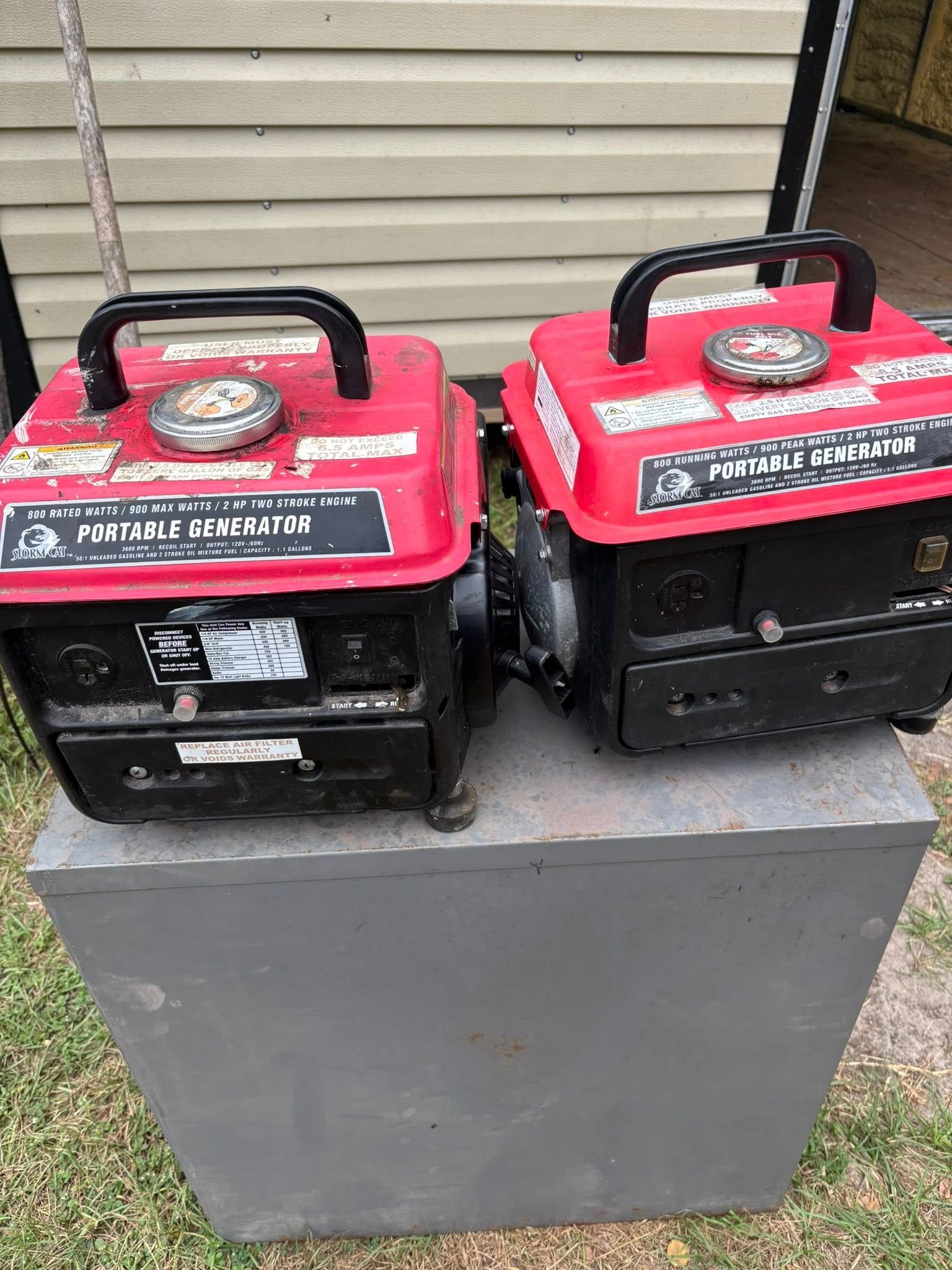 Two red and black portable generators on a gray box, outdoors.