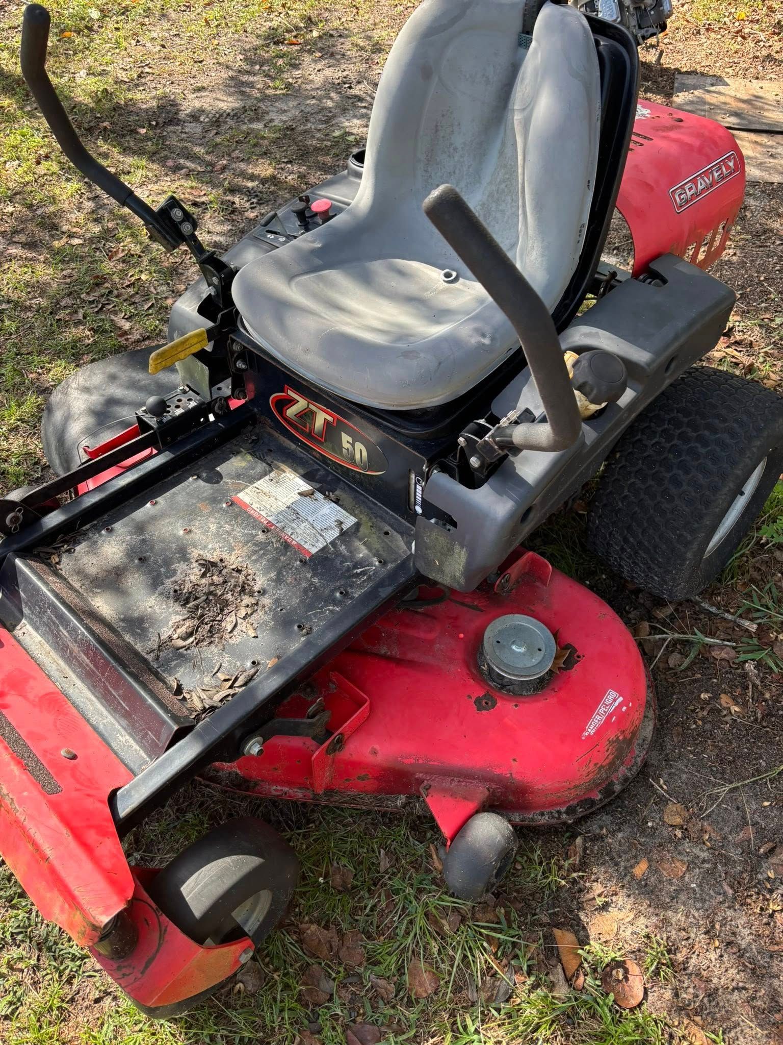 Red zero-turn lawn mower on grass with a dirty deck.