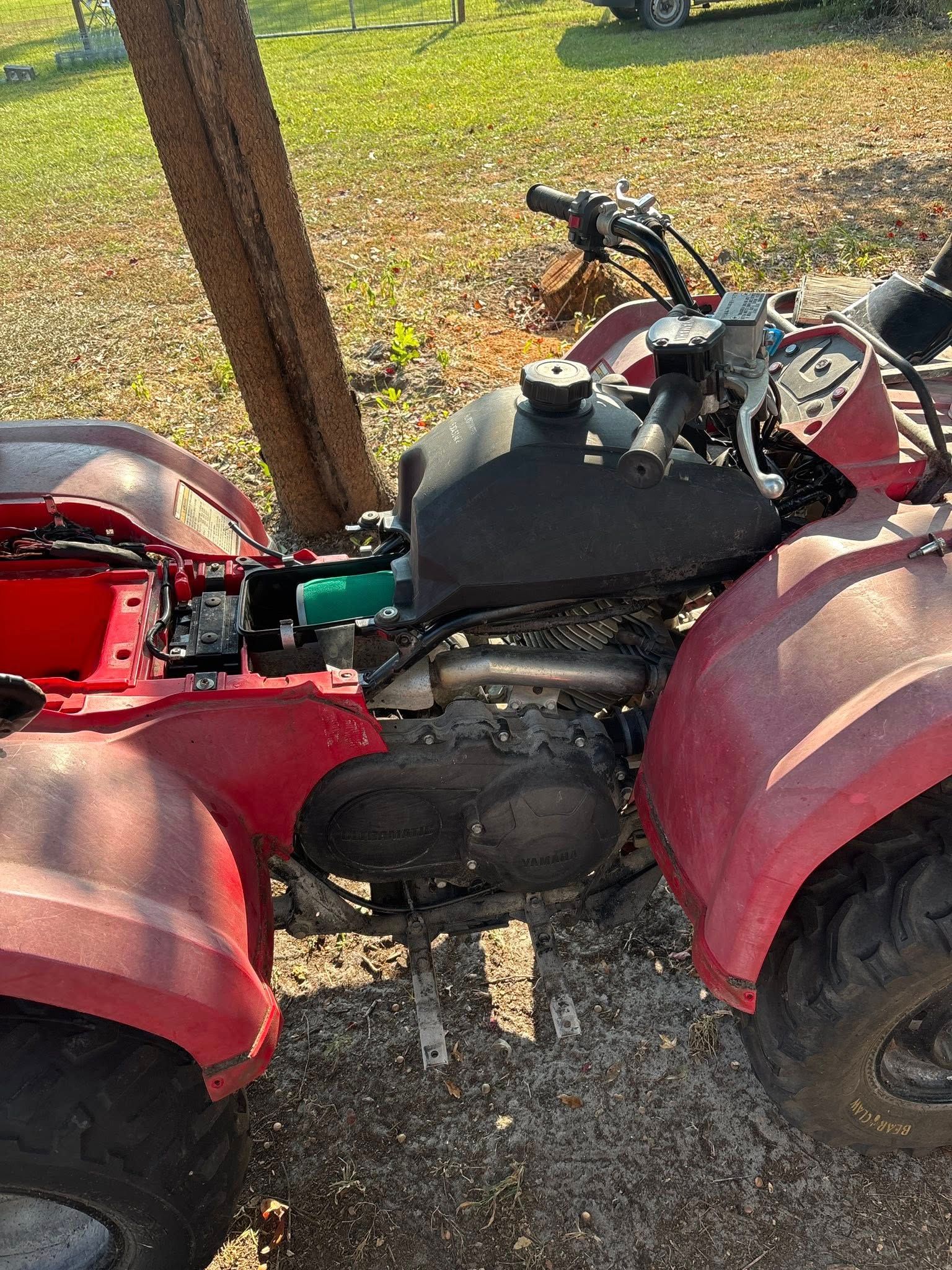 Red ATV parked near a tree in an outdoor setting.