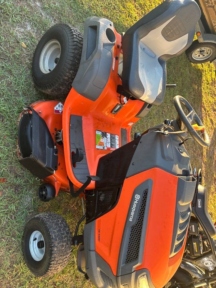 Orange Husqvarna riding lawn mower on grass, near a trailer.