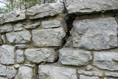 A man wearing gloves is working on a stone wall.