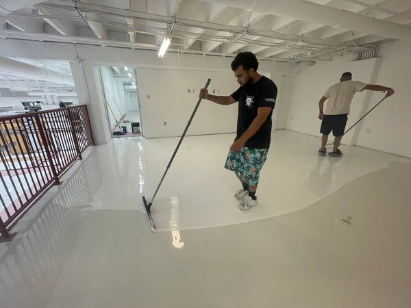 Two men are painting a white floor in a room