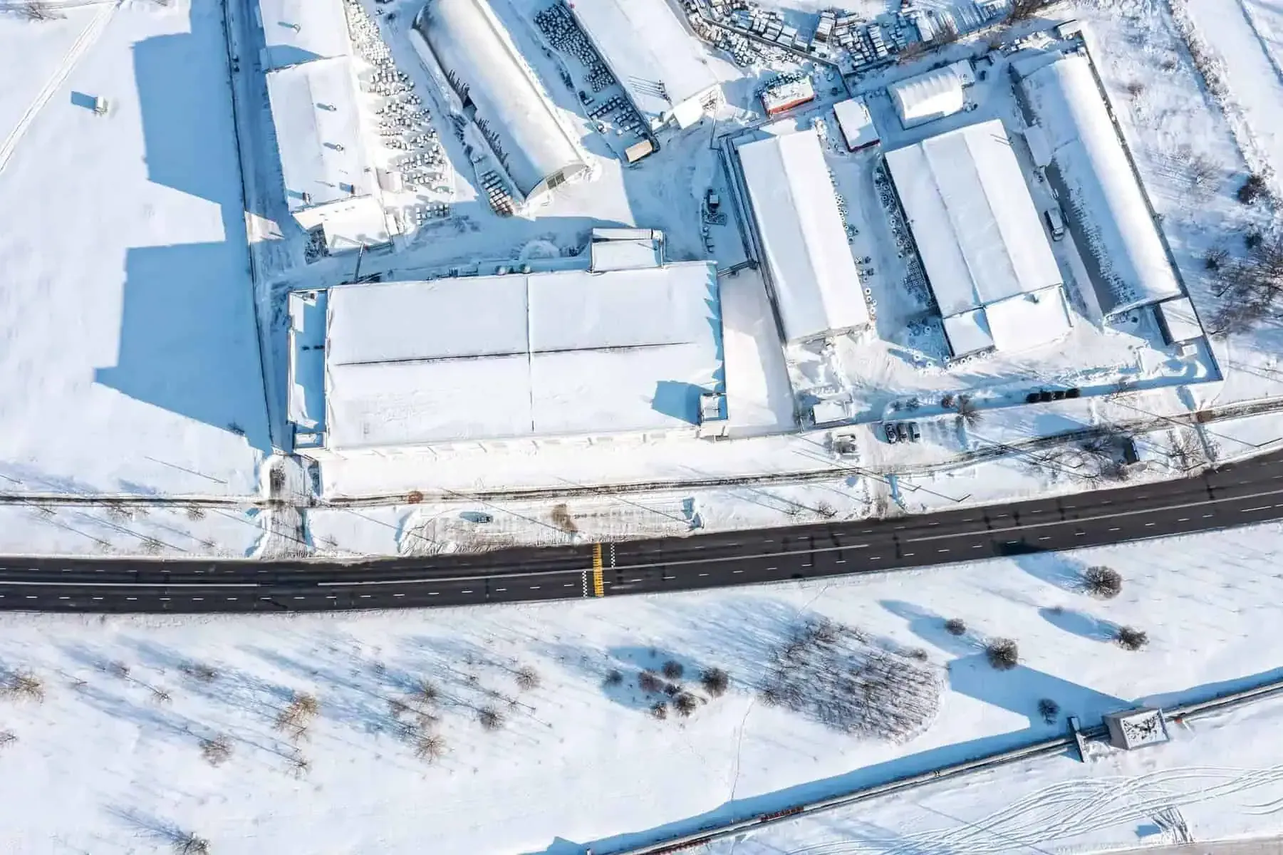 An aerial view of a snowy area with a road and buildings covered in snow.