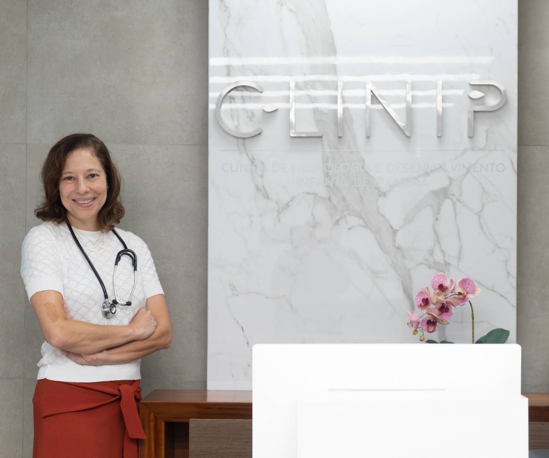Uma mulher com um estetoscópio no pescoço está parada em frente a uma placa que diz clínica.