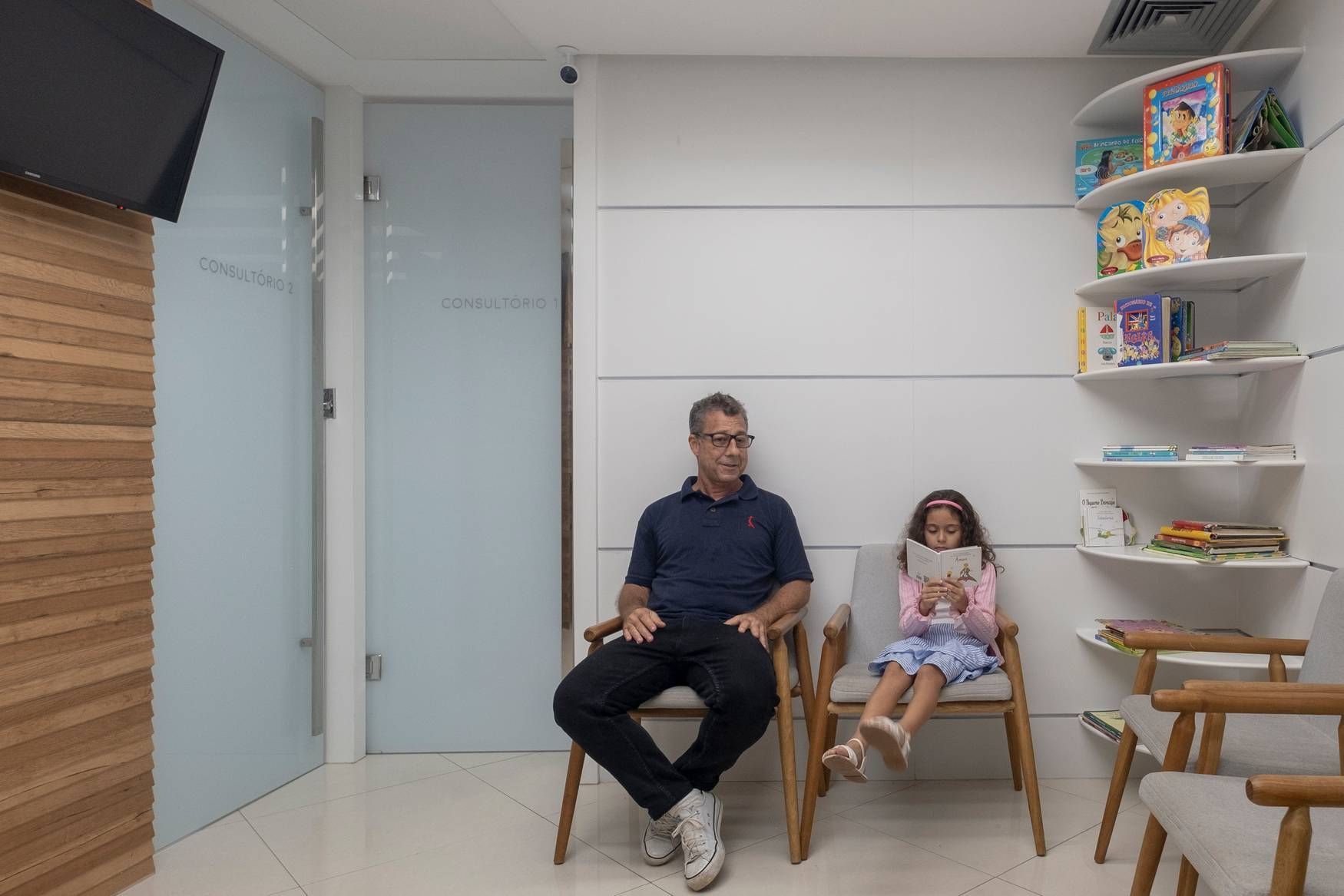 Um homem e uma menina estão sentados em cadeiras em uma sala de espera.