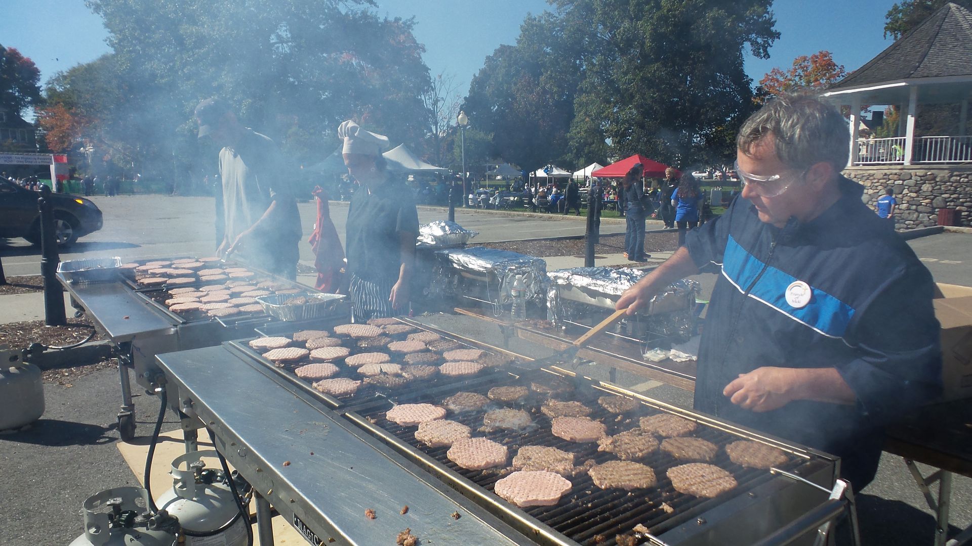 A man is cooking hamburgers on a grill outside